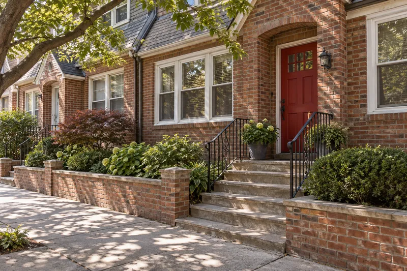 Illustrative Queens-style brick home with a red front door
